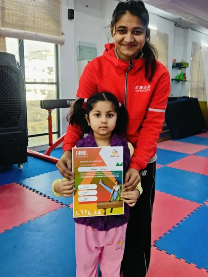 A very young gymnast proudly holds her "JUMP" certificate.