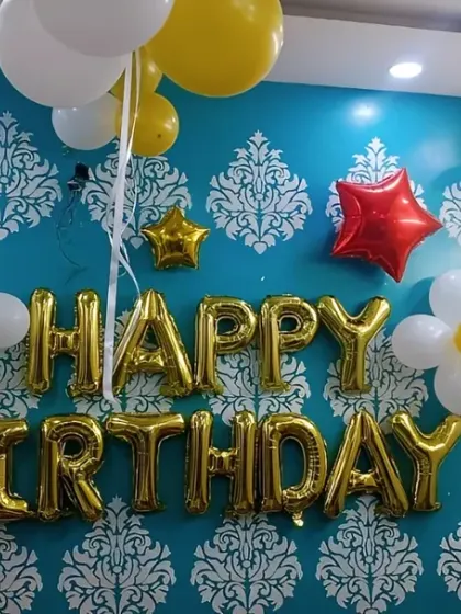 A cheerful birthday wall decoration with gold foil letters and balloon flowers in yellow and white.