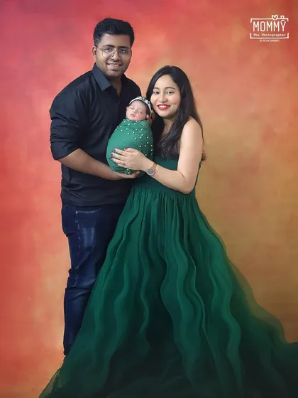 A beautiful family portrait with the new parents standing proudly with their baby. The mother's flowing green dress adds a touch of elegance and vibrant color.