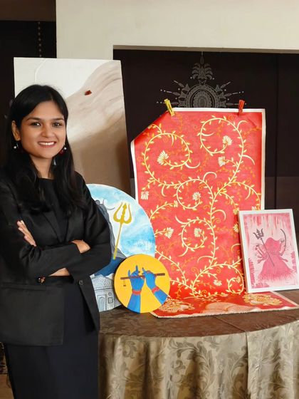 A proud moment with some of my finished pieces. You can see a variety of my work here, including a large red fabric piece with a golden vine pattern and smaller canvases with divine figures.