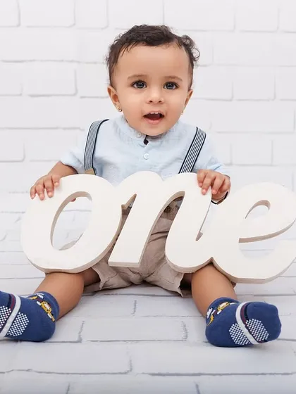 A cute toddler holds up a "one" sign, proudly announcing his first birthday.