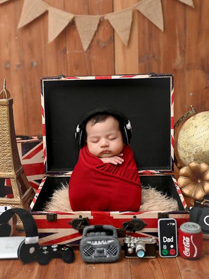 Ready for an adventure. This newborn is snugly wrapped in red and placed inside a vintage-style suitcase, surrounded by travel-themed props.