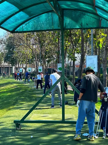 A golfer stands under the shade of a canopy, watching his shot on a busy weekend afternoon.