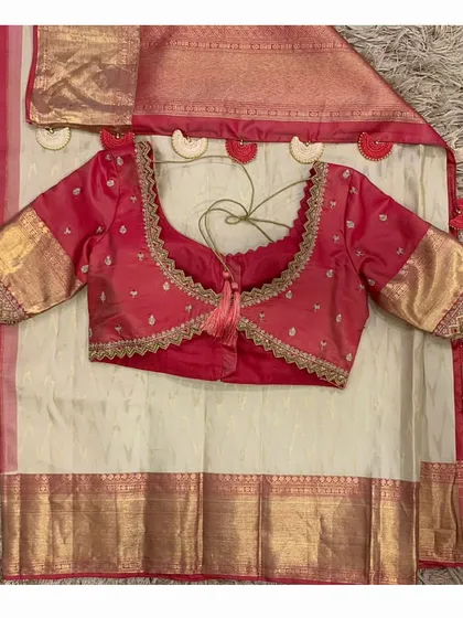 An elegant off-white silk saree with a red border, paired with a custom red hand-embroidered blouse. The saree is finished with unique heart-shaped tassels.