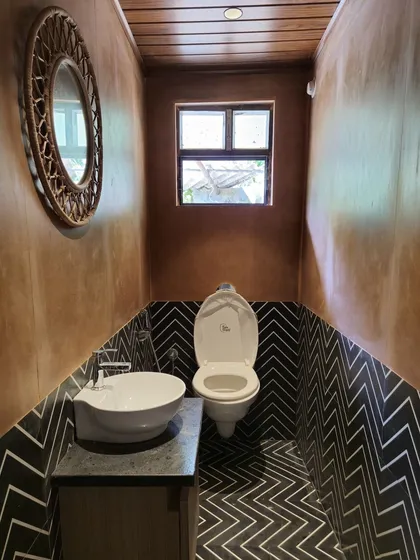 Even in compact spaces like this powder room, we focus on bold design choices. The dynamic black-and-white chevron tile floor is contrasted with warm, textured walls and a rustic woven mirror, creating a space with significant visual impact.