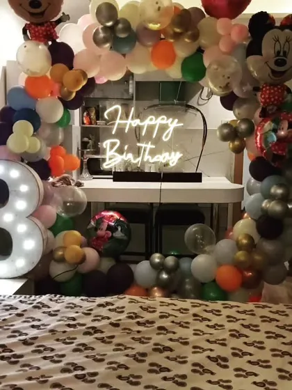 A Mickey and Minnie Mouse themed 3rd birthday. This decoration is set up in a room, featuring a balloon arch, a neon sign, and a large light-up number '3'.