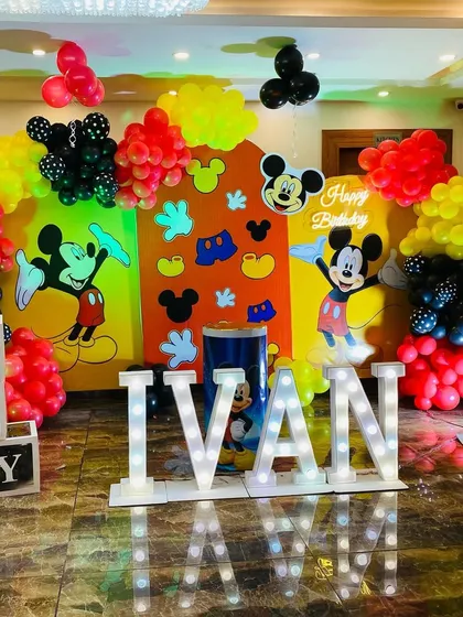 A classic Mickey Mouse themed first birthday for baby Ivan. The setup includes large marquee letters, character backdrops, and balloon arrangements in Mickey's signature red, yellow, and black colors.