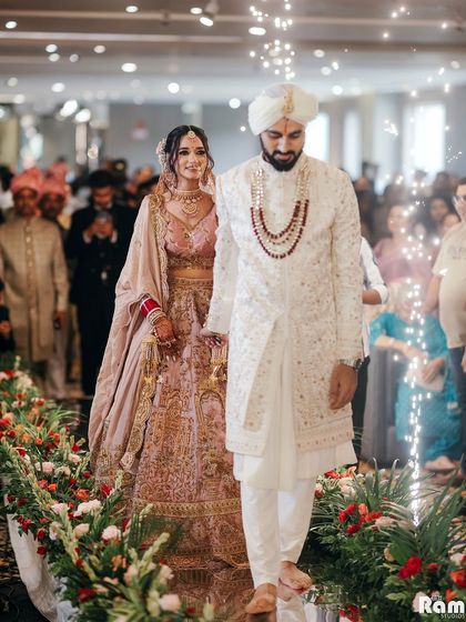 The couple's grand entrance into their wedding venue, walking down an aisle lined with flowers and pyrotechnics, hand-in-hand.