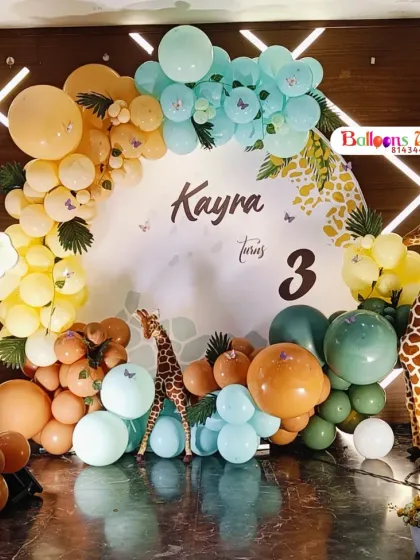 A detailed look at a safari-themed birthday for Kayra's third birthday. This setup includes a custom circular backdrop, a colorful balloon arch, and a variety of animal figures like a lion, giraffe, and zebra.
