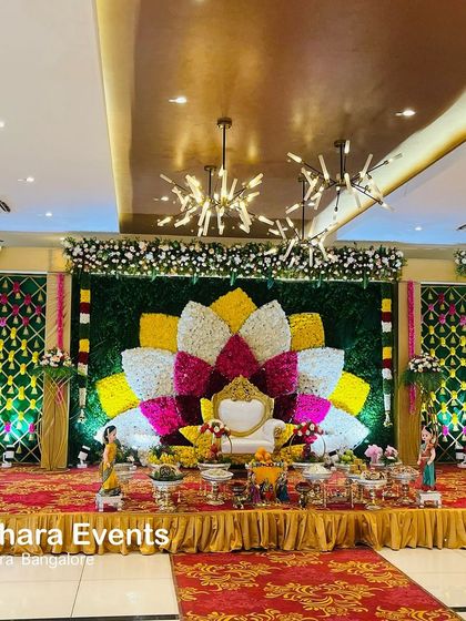 A grand Seemantham stage in a modern hall. The centerpiece is a large, multi-colored floral lotus, flanked by decorative panels, creating a stunning fusion of traditional and contemporary design.