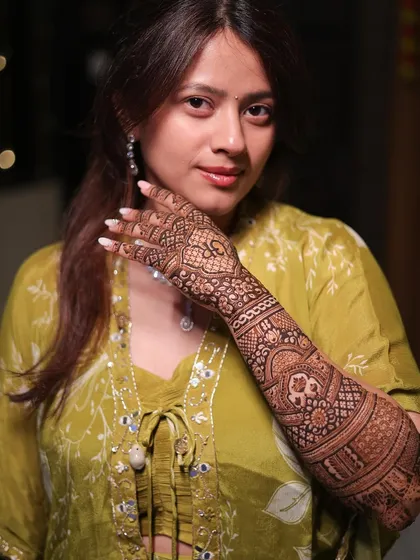 A portrait of the bride, beautifully showcasing her full-arm mehendi design. The intricate patterns complement her elegant green outfit perfectly.