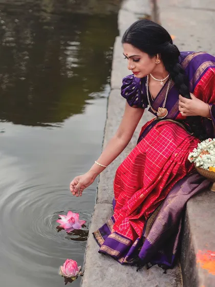 A gentle touch to a lotus flower in the temple pond. This beautiful, symbolic gesture is complemented by the elegance of the checkered red silk saree.