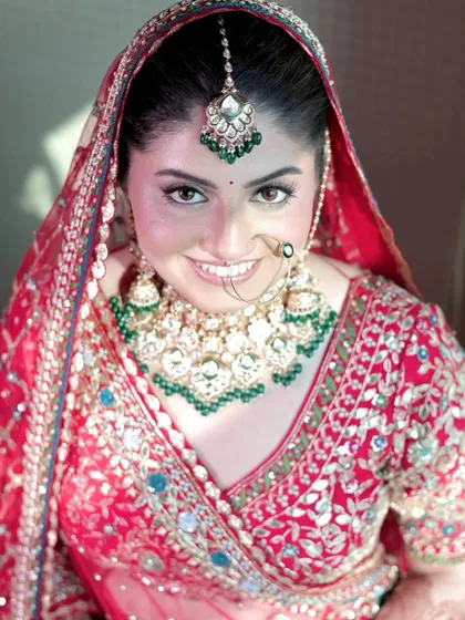 The smile of a happy bride says it all. She looks absolutely stunning in her red lehenga, and the kundan set with green accents she chose from my collection was the perfect finishing touch.
