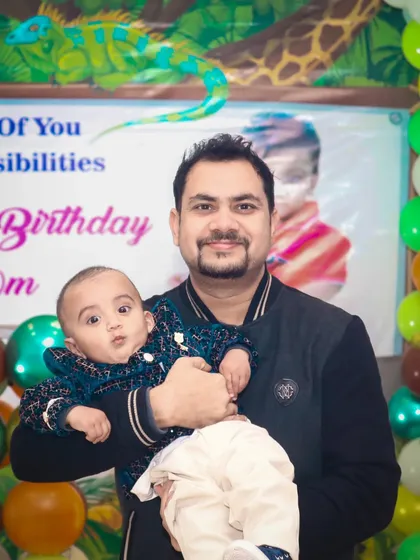 A father proudly holds his baby boy at a birthday party. I capture many father-child moments that families cherish.