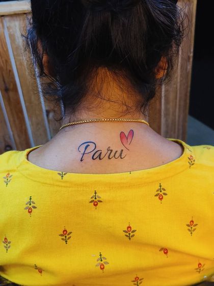 A "Paru" name tattoo placed on the back of the neck, finished with a small, color-filled heart. This is a popular and discreet placement for a personal tattoo.