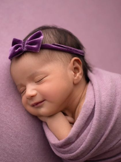 Another precious sleepy smile. The simple purple wrap and bow keep the focus entirely on her adorable expression.