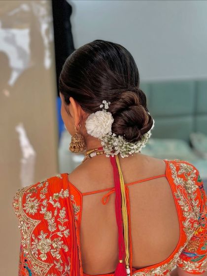A sleek and modern bun adorned with white flowers, perfect for a bride in a vibrant, contemporary lehenga.