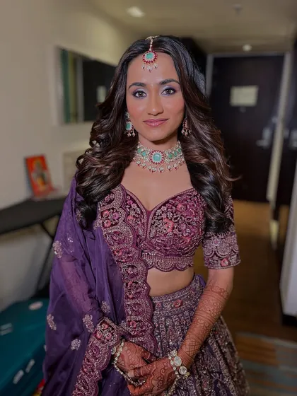 A full-length shot of a bride ready for her reception. She chose a beautiful zircon necklace with mint-colored stones to match her unique purple lehenga, and the result is pure elegance.