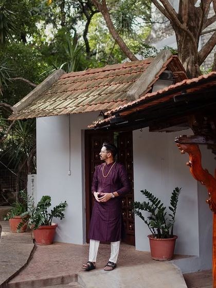 The groom stands on the porch of a suite, the traditional architecture and lush surroundings creating a handsome and classic portrait.