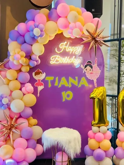A ballerina-themed 10th birthday party. This setup includes a purple backdrop, ballerina cutouts, a "Happy Birthday" neon sign, and a pastel balloon arch.