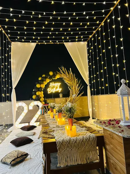 A view of our terrace dinner setup under a canopy of fairy lights. This image highlights the low seating arrangement with a macrame table runner and candles, perfect for an intimate birthday dinner.