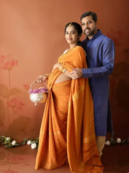 A full-length portrait of a couple in traditional attire against a painted lotus backdrop, perfect for a cultural maternity photoshoot.