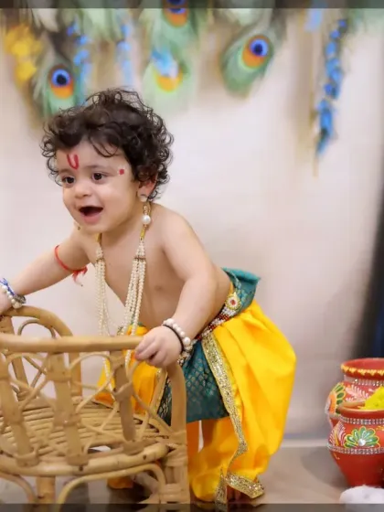 This little boy is all smiles during his Krishna photoshoot, surrounded by props like a miniature wicker cradle and colorful pots.