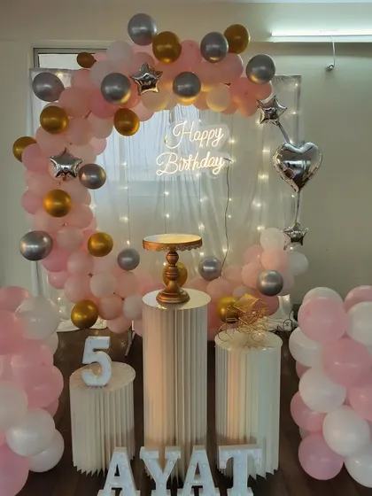 A soft pink, silver, and gold balloon arch with a sheer curtain and fairy lights for a dreamy effect.