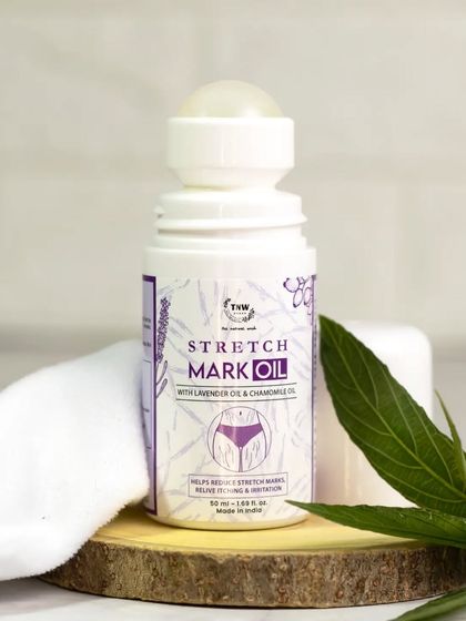 A stretch mark oil is presented on a rustic wooden slice with a clean white cloth and a green leaf. The natural elements in this shot emphasize the product's gentle, plant-infused ingredients.