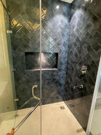 A look inside the shower cubicle, highlighting the rich texture and color variation of the dark grey tiles laid in a classic herringbone pattern.