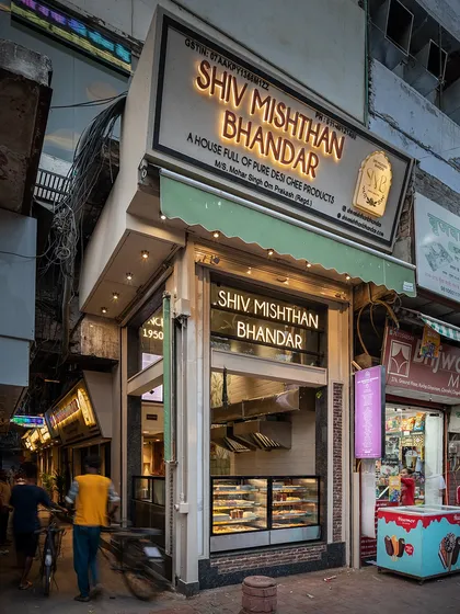 The exterior of Shiv Mishthan Bhandar at dusk. The material palette, including red stone and lakhori bricks, was inspired by the architecture of Chandni Chowk's havelis to ground the modern storefront in its context.