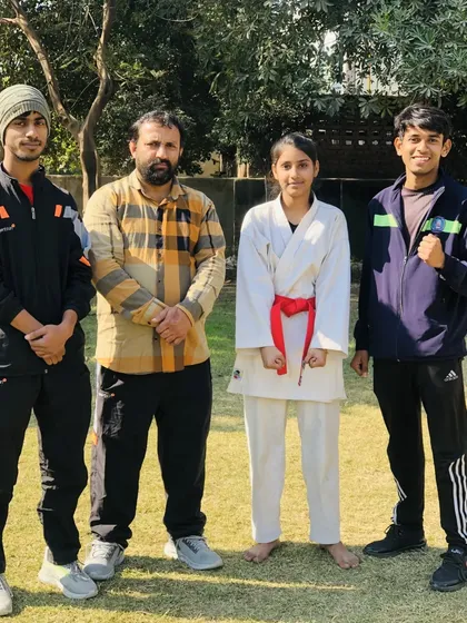 A student in her karate gi, standing with the coaching team. She has shown great progress and discipline.