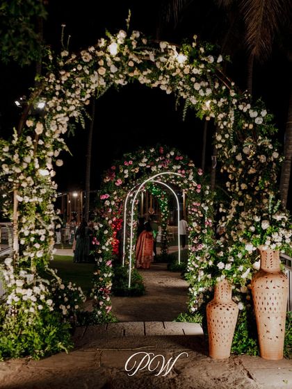 A floral wonderland for a Sangeet night. This entrance features a series of arches covered in white and pastel flowers, creating a dreamy pathway for guests.