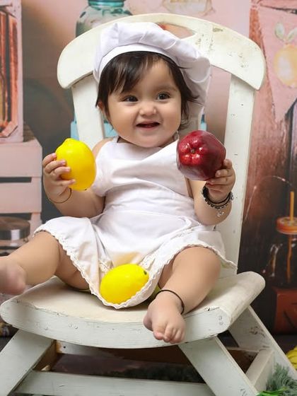 This little chef is ready to cook up some fun for his first birthday. The combination of a chef's hat, toy fruits, and a rustic background makes for a playful and memorable milestone photo.