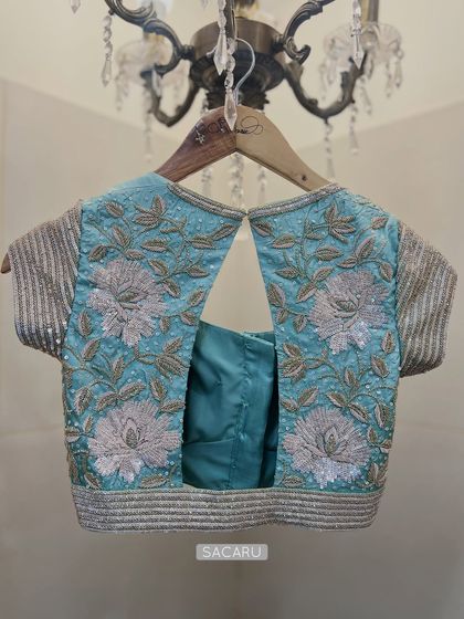 A sparkly floral embroidered blouse in a combination of light gold and silver detailing on a powder blue base, with a stylish back cutout.