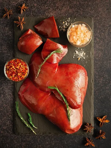 A flat lay of raw liver on a dark slate, garnished with fresh rosemary and surrounded by spices. The composition is clean and artistic, elevating a simple raw ingredient into something beautiful.