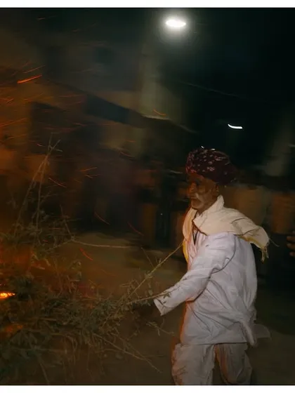 An elderly man participates in the Holika Dahan fire ritual in a village near Jodhpur. The motion blur and fire create a dynamic and spiritual atmosphere.