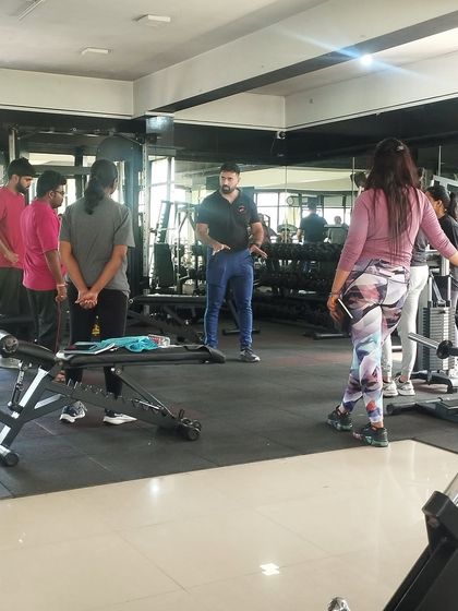 A master trainer addresses a group of students in the weights area, explaining the principles of a new exercise.