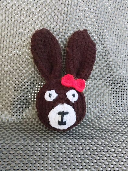 A crochet teddy bear face applique, which can be used in various craft projects or as part of a bouquet.