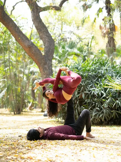 A beautiful side-star acroyoga pose, requiring core strength and balance from both partners, set in a peaceful park.