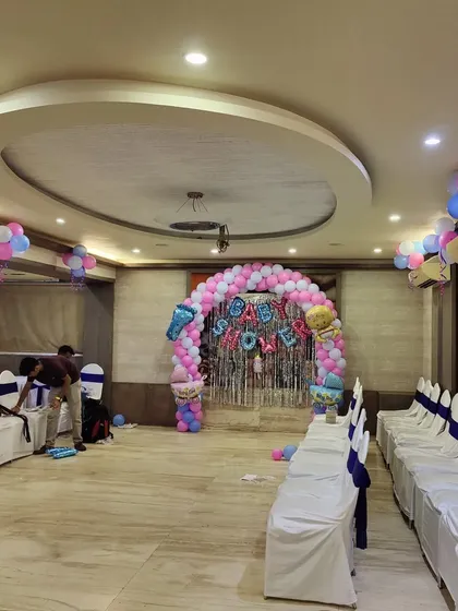 This photo shows a full view of a banquet hall decorated for a baby shower. You can see how the main balloon arch at the stage is complemented by matching chair sashes and balloon clusters throughout the room.