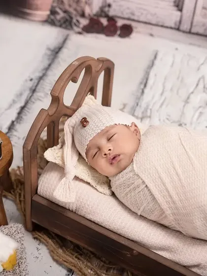 Tucked into a tiny wooden bed, this swaddled newborn is fast asleep. The miniature lantern and sleeping puppy prop add a charming, storybook quality to the scene.