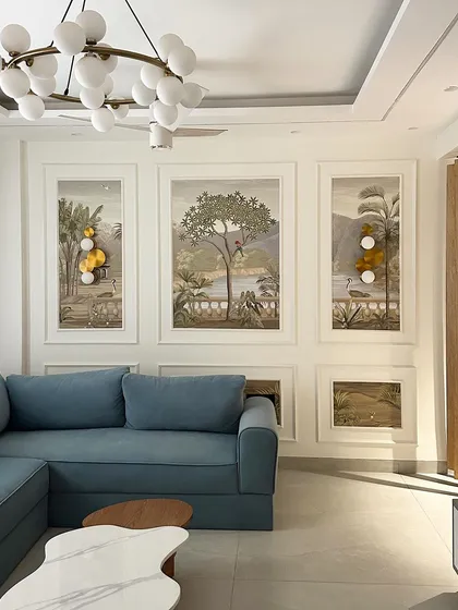 This living room design uses framed scenic wallpaper panels as art, complemented by a comfortable blue L-shaped sofa for a serene and artistic feel.
