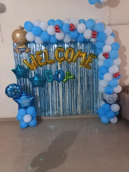 A 'Welcome Boy' balloon arch with a blue fringe curtain. The arch is decorated with star and baby-themed foil balloons.