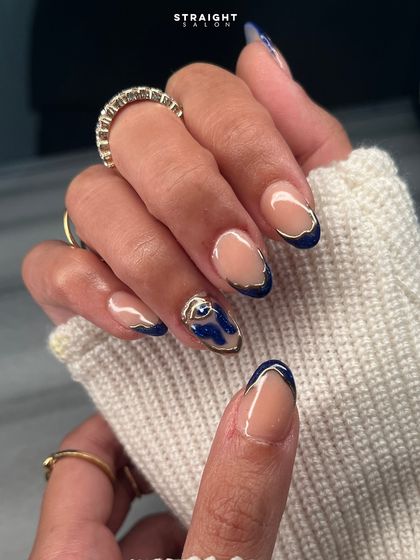A modern twist on a French manicure, featuring a deep blue tip with a hand-painted gold outline and a 3D abstract blue and gold accent nail.