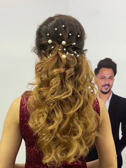 A half-up, half-down hairstyle with soft curls and a pearl-studded top section, created during a live demo at a beauty expo.