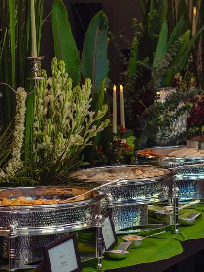 A wide view of our luxurious buffet line, framed by tall floral arrangements and candlelight. We use stunning serveware and decor to elevate the traditional buffet into a fine-dining experience.
