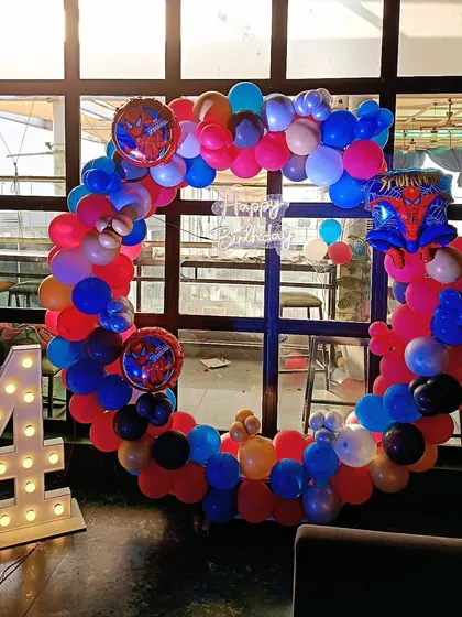 This circular balloon arch with a Spiderman theme is a popular choice for kids' parties hosted at restaurants, featuring vibrant colors and a light-up number '4' for the birthday.