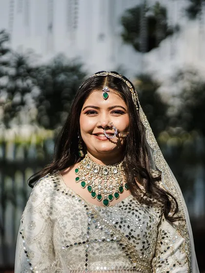 A close-up of pure bridal radiance. The intricate mirror work and gotta pati detailing on this ivory lehenga catch the light beautifully, framing her happy smile.