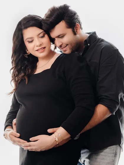 A warm and affectionate studio portrait of an expecting couple. The partner embraces the mom-to-be from behind, both sharing a gentle smile, creating a feeling of comfort and love.